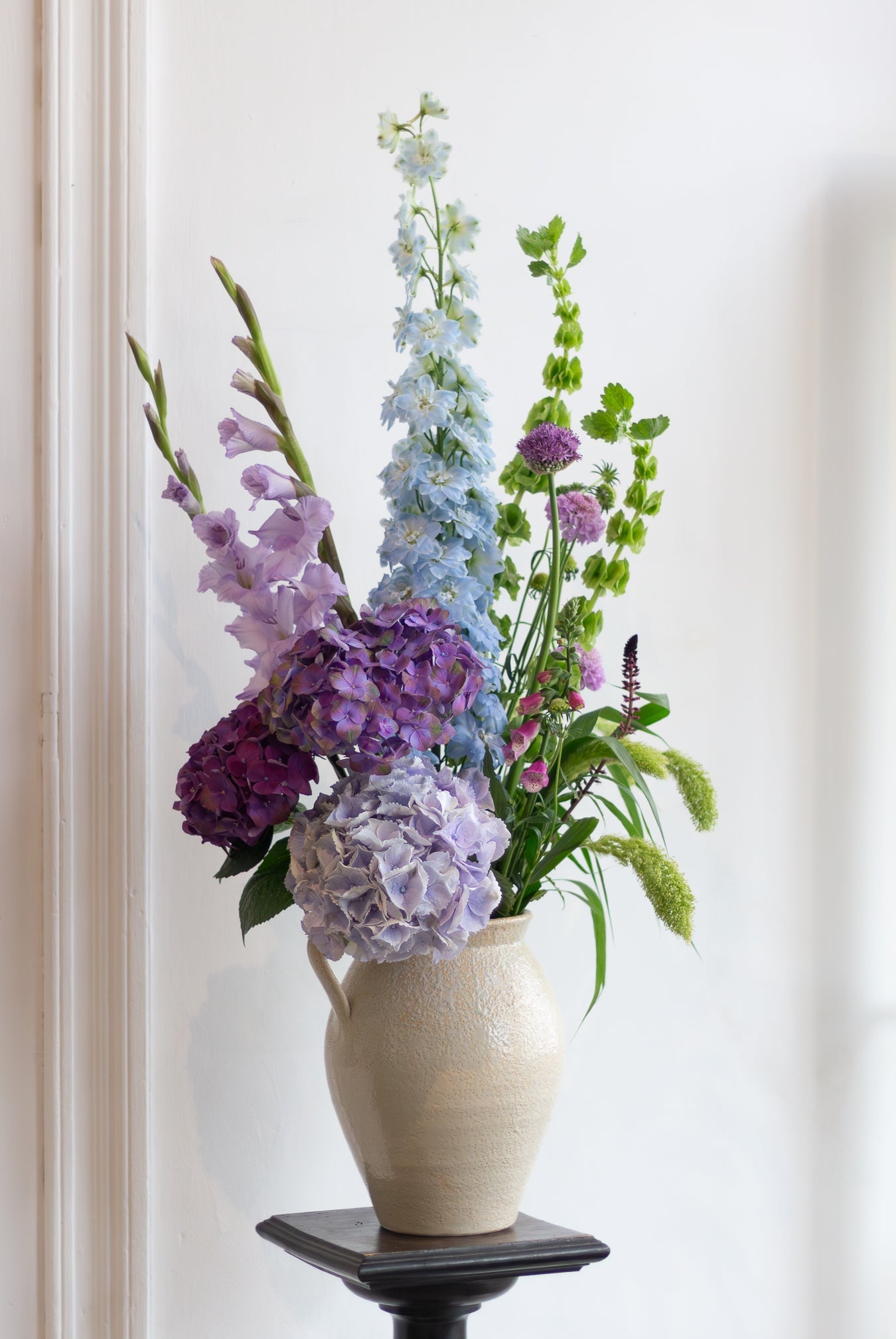 Vase with colorful flowers on a stand against a white wall