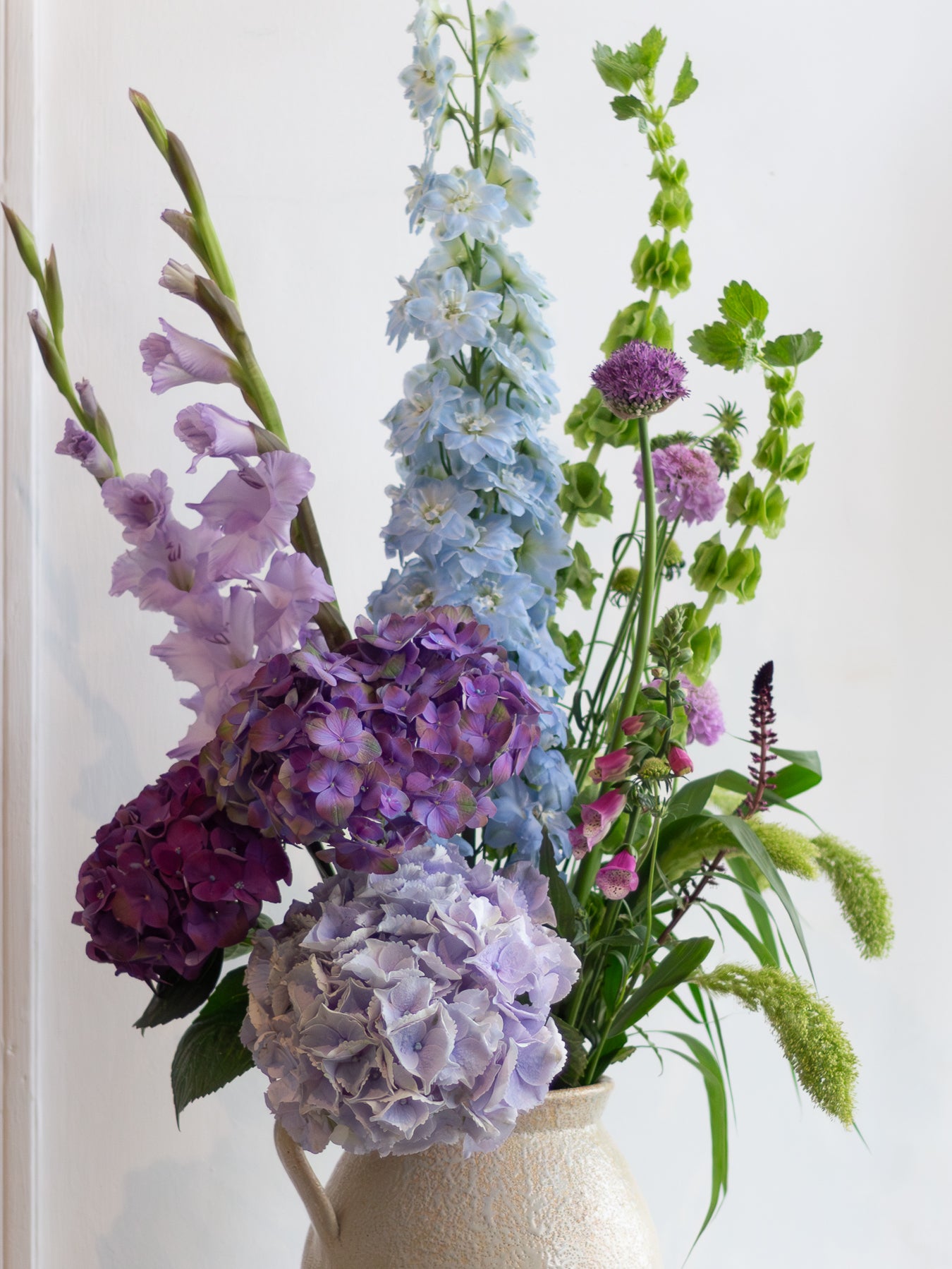 Vase with a bouquet of flowers including purple, blue, and green elements on a white background